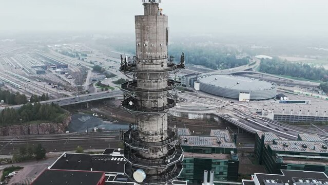 Aerial medium shot of a bleak industrial concrete television and radio link tower in Pasila, Helsinki, Finland on a bright and foggy day. Camera orbiting around,  Arena and railways in background.
