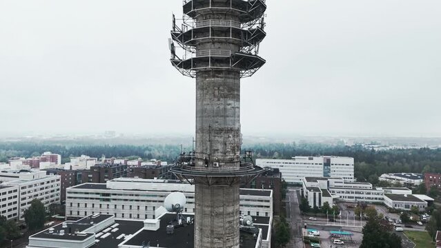 Aerial medium shot of a bleak industrial concrete television and radio link tower in Pasila, Helsinki, Finland on a bright and foggy day. Camera ascending, apartment buildings in background.