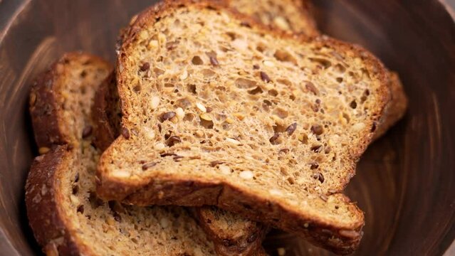 Falling slice of rye whole grain cereal bread with crunchy crust into a rustic dark wooden bowl close up in slow motion