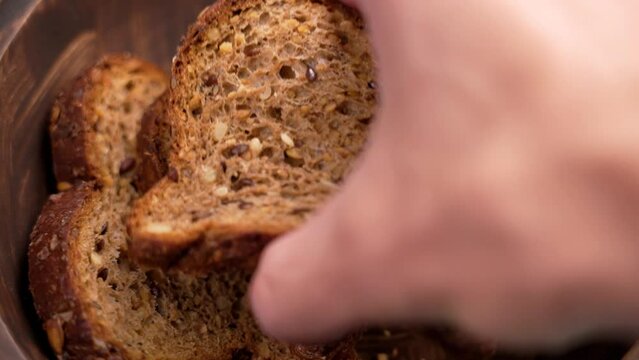 Hand takes a slice of cereal rye bread made from dark flour close up