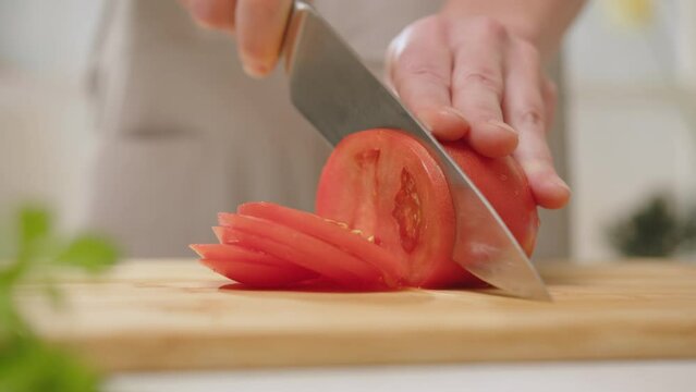 Woman hands slicing fresh tomato with knife on cutting board in kitchen. Cooking healthy food from vegetables.