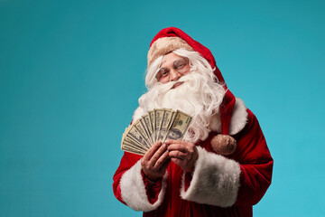 portrait of Santa Claus holding money dollars in his hands on a clean blue background, Santa gives...