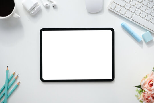 The top view image of white workspace is surrounding by a white blank screen tablet and various equipment.