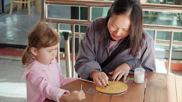 Korean Mother with Mixed Daughter Playing Korean Traditional Game Scratch Dalgona Sugar Caramel Candy with Toothpick in Shape of Triangle, Heart and Pine Tree at Gyeongamdong Railroad Town Old Market
