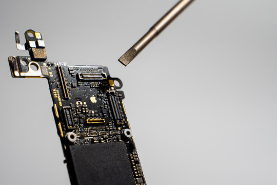 Kyiv, Ukraine - August 25, 2023: A screwdriver points to the golden Apple logo on the iPhone SE motherboard, close-up