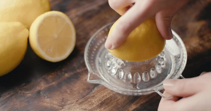 Female hand squeezes fresh lemon juice on glass squeezer in close up