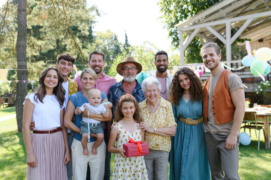 Family portrait at outdoor summer garden party. Family and friends standing, posing for a group photo. Multigenerational family.