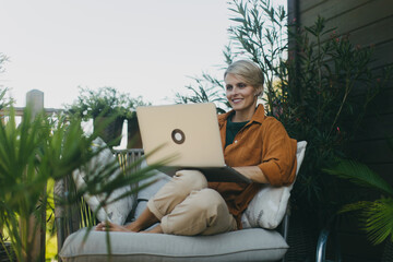 Woman in the garden working on laptop, sitting on patio chair. Businesswoman working remotely from...
