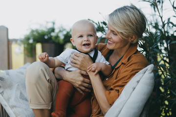 Beatiful mother sitting with little son outdoors, in garden patio. Warm autumn day of mother with...