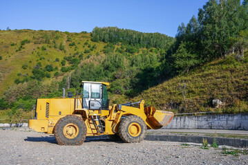 A tractor stands on a gravel road in the mountains