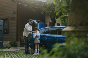 Portrait of a man charging electric car in front of his house, plugging the charger into the...