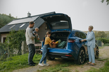 Family with electric car standing in front their house with solar panels on roof. Solar energy and sustainable lifestyle of young family. Concept of green energy and sustainable future for next