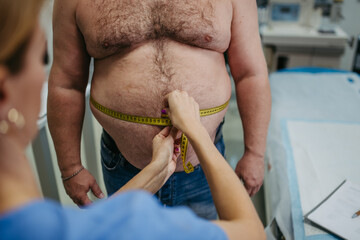 Female doctor measuring waist of overweight patient using tape measure. Obesity affecting...