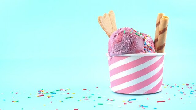 scoops of berries ice cream in bowl with strewed sprinkles, cigars and cookies on blue background, summer creative concept, copy space