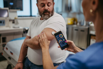 Doctor connecting continuous glucose monitor with smartphone, to check blood sugar level in real time. Obese, overweight man is at risk of developing type 2 diabetes. Concept of health risks of - obrazy, fototapety, plakaty