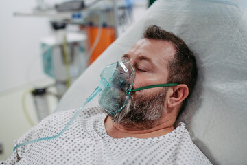 Unconscious patient with oxygen mask on hospital bed. Man in intensive care unit in hospital.
