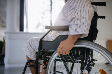Obraz premium Side view of man in wheelchair. Overweight patient in hospital gown waiting for medical examination in hospital.