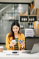 Asian Woman using smart phone for mobile payments online shopping, omni channel, sitting on table, virtual icons graphics interface screen .