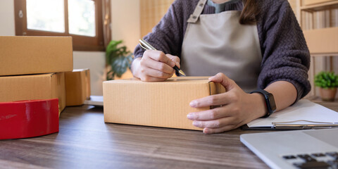 Woman is writing a list of customer on box before shipping to them, she runs an ecommerce business on websites and social media. Concept of selling products online