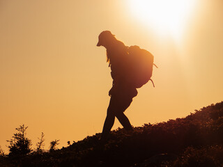 Silhouette of hiker tourist woman with backpack during mountain trekking from the top.