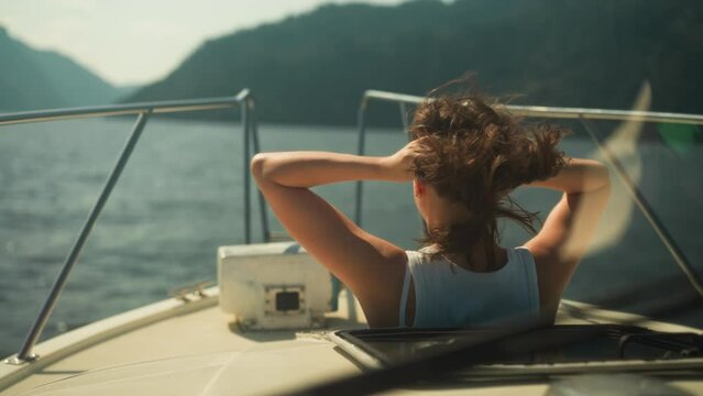 Woman with hair disheveled from wind looks out of open hatch of cabin on motorboat sailing on lake. Relaxation and scenic view in warm weather