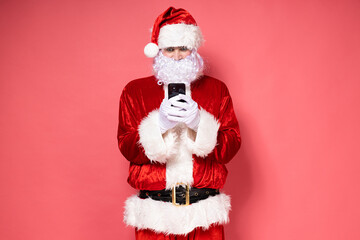 Santa Claus with a phone on a pink background.