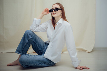 A young beautiful girl is sitting in black glasses and a white shirt