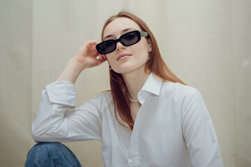 A young beautiful girl is sitting in black glasses and a white shirt