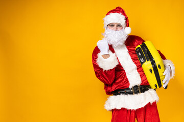 Fototapeta na wymiar Santa Claus, with a yellow suitcase in his hands, on a yellow background.