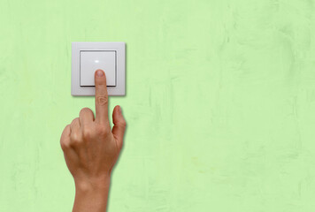 Female finger on light switch close-up, green background.