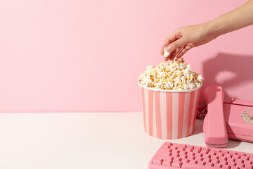 Popcorn in paper cup, devices and hand on pink background, space for text