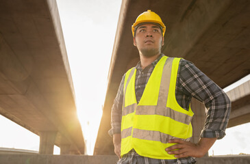 Expressway construction engineer in relaxed pose holding a yellow helmet under construction site