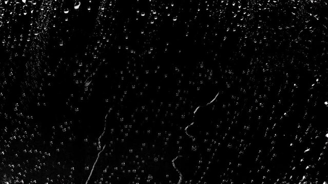 Slow motion drop of rain falls on the window of a black background rainstorm textured pattern natural raindrop plane effect particles abstract light macro texture close up