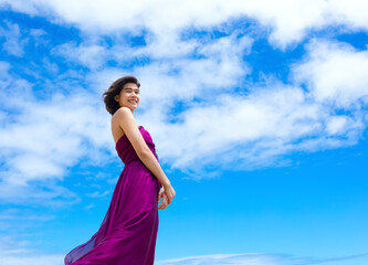Obraz premium Teen girl in purple dress standing against blue skies
