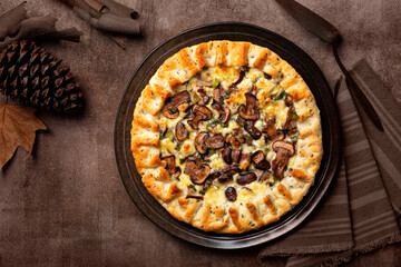 Autumn savory pie. Mushroom, cheese, green onion and spinach open pie or galette. Homemade bakery. Top view, brown background with fall dried plants.