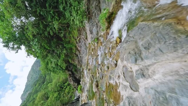 Vertical drone shot over flowing rocky river with waterfall and green tropical rainforest in Dominican Republic 