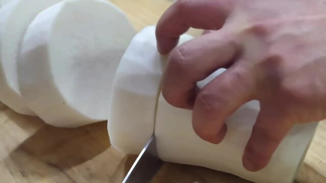 Watch a chef's quick mastery as they expertly cut daikon radishes and leeks with precision in a restaurant kitchen, showcasing their knife skills