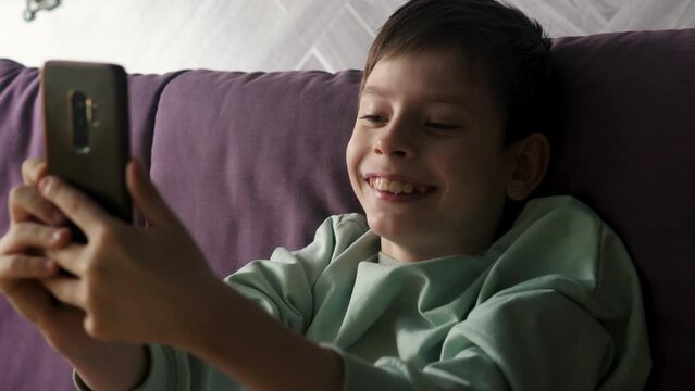 Caucasian child, little boy. happy child lying upside down on the sofa using a mobile phone. Schoolchild leisure concept.