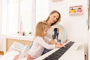 Little girl playing a piano with her mother