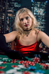 Pretty girl in red shiny dress and hat playing poker at casino