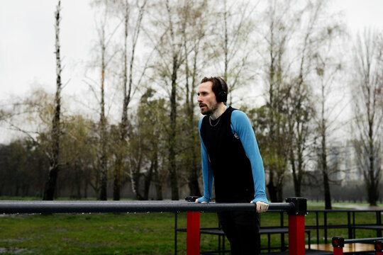 Sportsman sets a record for pushups parallel bars. Concentrated man listen music headphones while balancing. Adult athletic guy exercise crossfit using metal equipment on court. Workout motivation