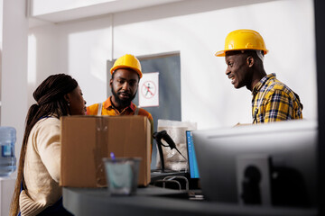 Delivery service employees discussing packages storing at warehouse reception desk. All black postal storehouse men and woman workers team having communication at storage room counter