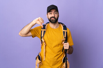 Caucasian handsome man with backpack and trekking poles over isolated background showing thumb down with negative expression