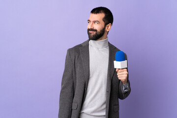 Adult reporter man with beard holding a microphone over isolated purple background having doubts...