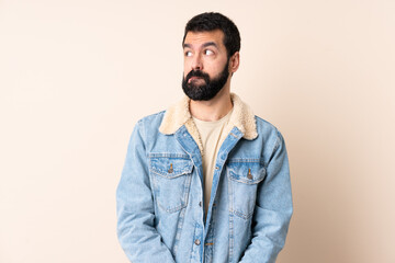 Caucasian man with beard over isolated background having doubts while looking up