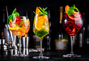 Red, white, pink sangria cocktail drinks with spanish wine, fruits, citrus and ice. Black bar counter background, steel bar tools and bottles