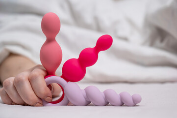 Woman holding three different anal beads while lying in bed. 