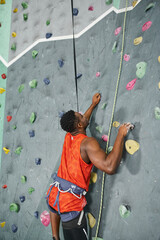 vertical shot of african american man ascending up bouldering wall and looking up, sportsman