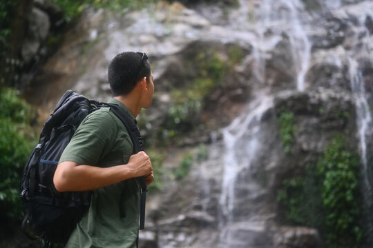 Image of male hiker with backpack enjoying the view of beautiful tropical waterfall