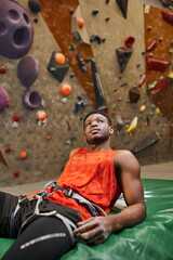 vertical shot of relaxed african american man after climbing rock wall chilling on crash pad